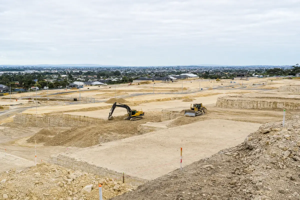 Bulk earthworks across a Perth land subdivision with graded sand pads, limestone cut faces and an excavator working