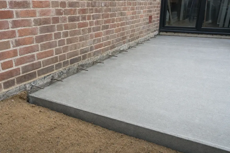 New concrete slab poured against the existing brick wall of a Perth house with starter bars at the construction joint
