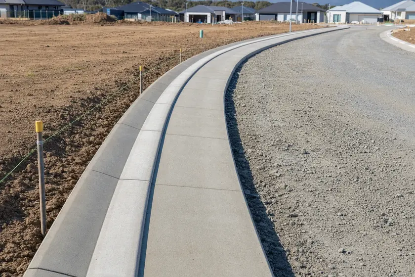 Freshly poured concrete kerb and gutter beside compacted road base on a new residential road