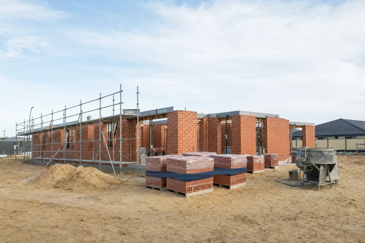 Perth double-brick house at brickwork stage with scaffolding, brick packs and a mortar station on the sand pad