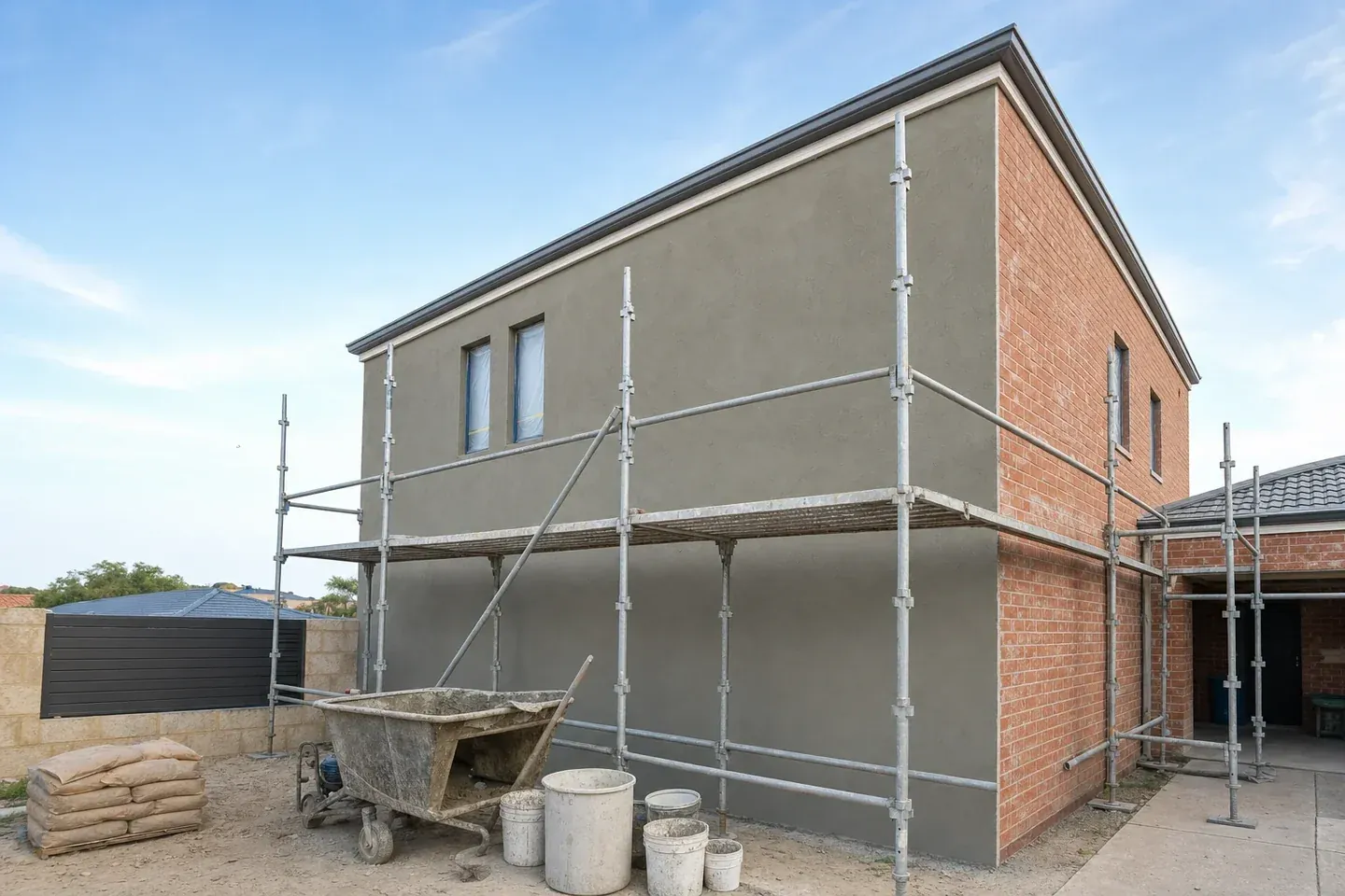 Perth house part way through rendering with scaffolding, one elevation coated in base render and the next still bare brick