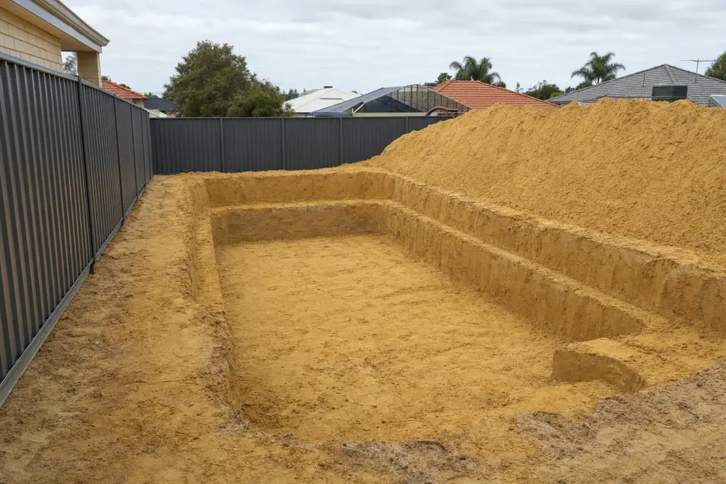 Battered sand excavation for a swimming pool in a Perth backyard with spoil stockpiled beside the cut